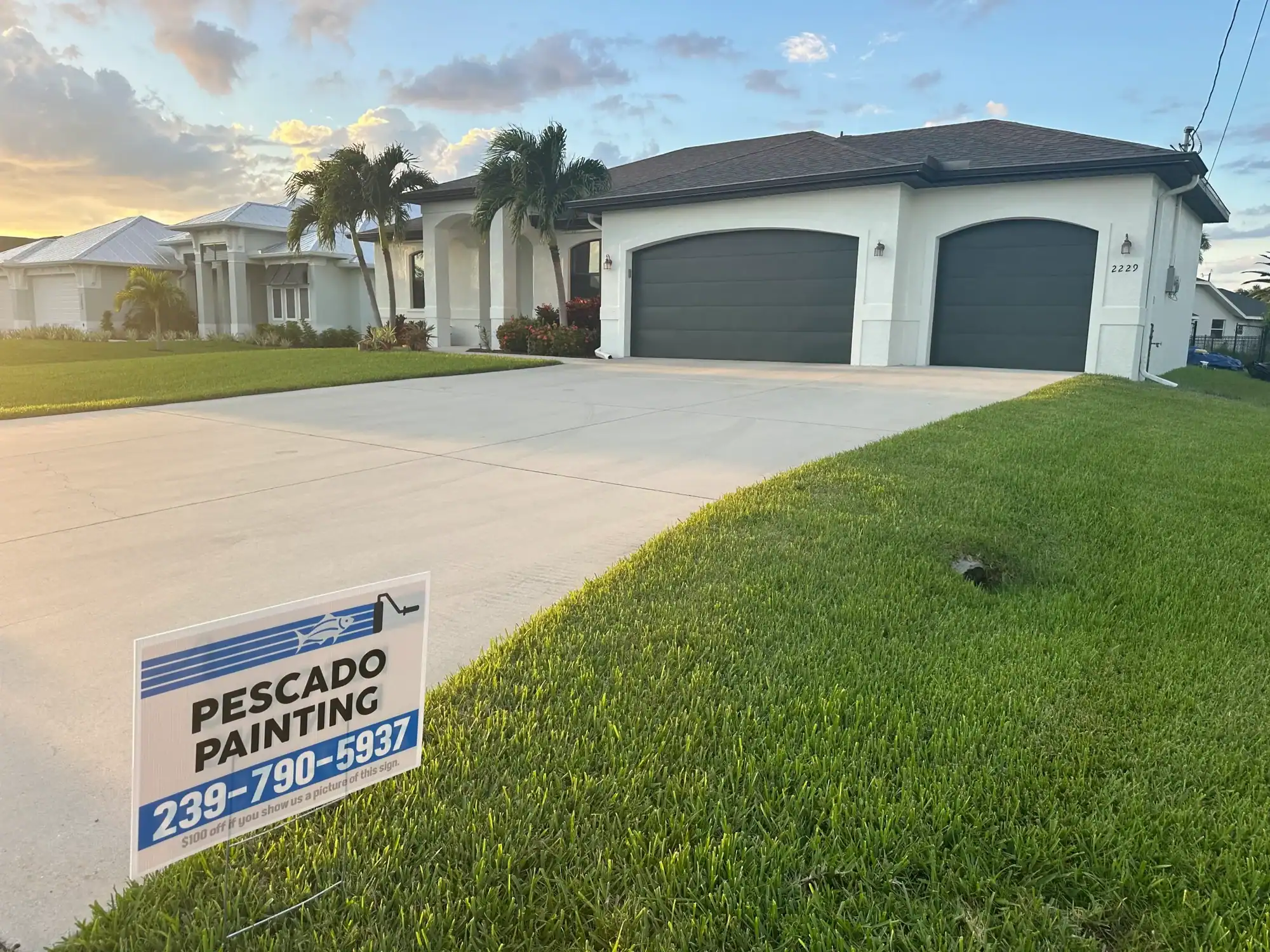 Modern white house with dark gray garage doors and a Pescado Painting sign in the foreground in Southwest Florida.