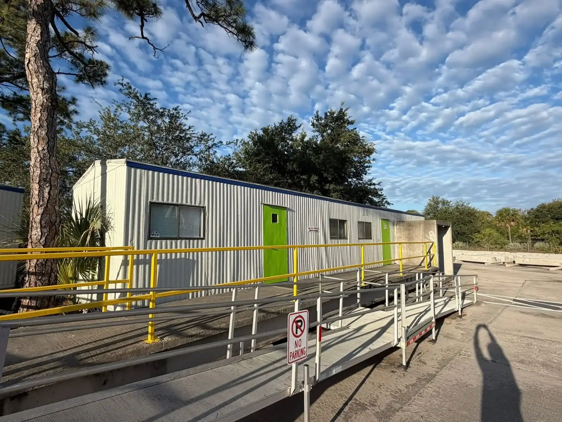 Commercial Metal Building Painting in Southwest Florida A white corrugated metal commercial building with a bright green door and yellow ramp in Southwest Florida.