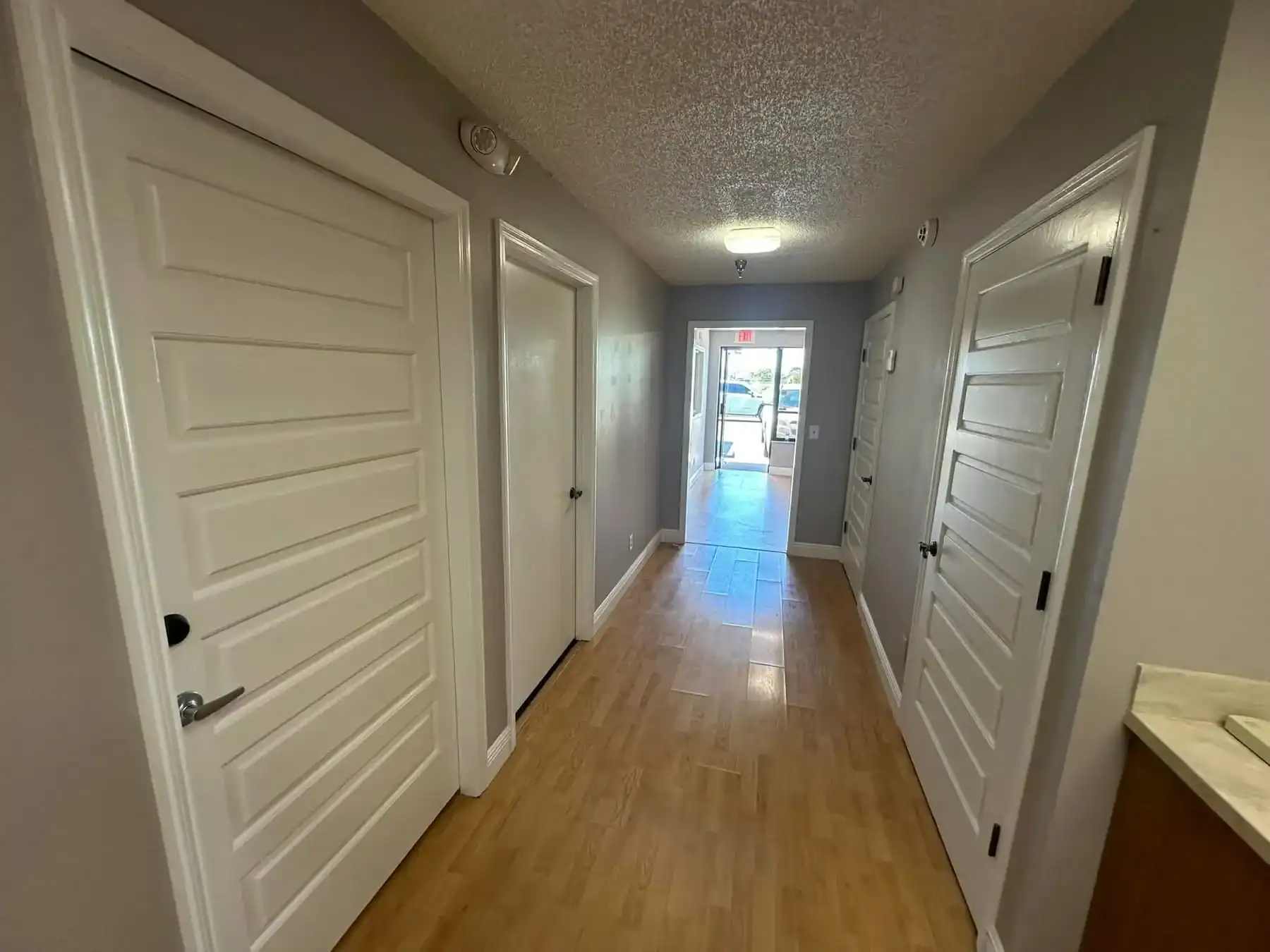 Apartment or Office Hallway Interior Painting Southwest Florida Long interior hallway with light gray walls, multiple white doors, and wood laminate flooring in Southwest Florida.